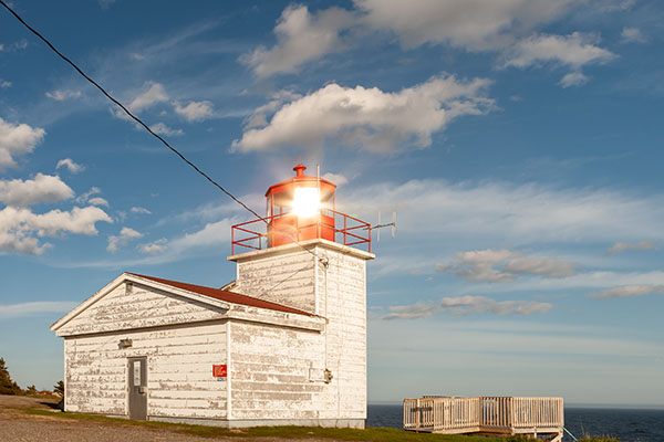 A small lighthouse during the day with the sun reflecting off the light housing.
