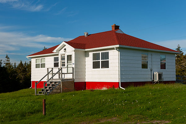 The exterior of a small cottage painted white with red trim.