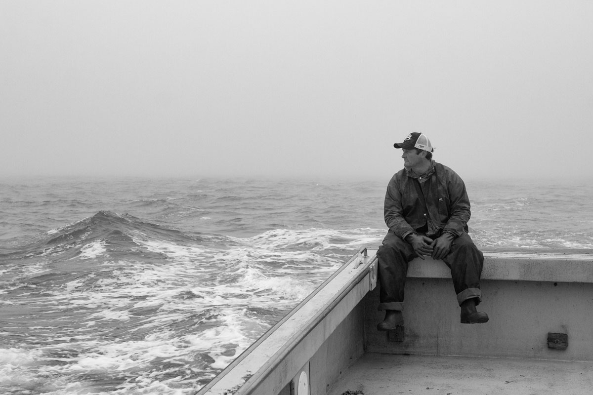 A lobster fishermen sits on the stern of his boat as it sails to the next trap.